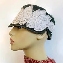 Load image into Gallery viewer, One of a kind design elements and embellishments upcycled from salvaged remnant fabric scraps, and hand sewn in Santa Cruz, CA. 100% cotton cap, handmade in Bali.   Off white &quot;leaf&quot; shapes and earth brown stitches   Army green colored cap Button embellishment 100% cotton US size 7 1/8&quot; *  Wash cold, hang dry *see size chart for detailed measurement
