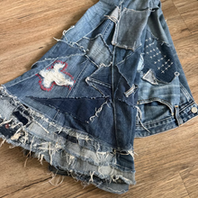 Load image into Gallery viewer, Denim skirt with patches and frayed edges on a wooden floor
