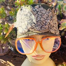 Load image into Gallery viewer, One of a kind, design elements and embellishments upcycled from salvaged remnant fabric scraps, and hand sewn in Santa Cruz, CA. 100% cotton cap, handmade in Bali.   Brown corduroy and &quot;cracked playa&quot; fabric   Army green colored cap Adorned with several different feathers  100% cotton US size 7 1/4&quot; *  *see size chart for detailed measurement
