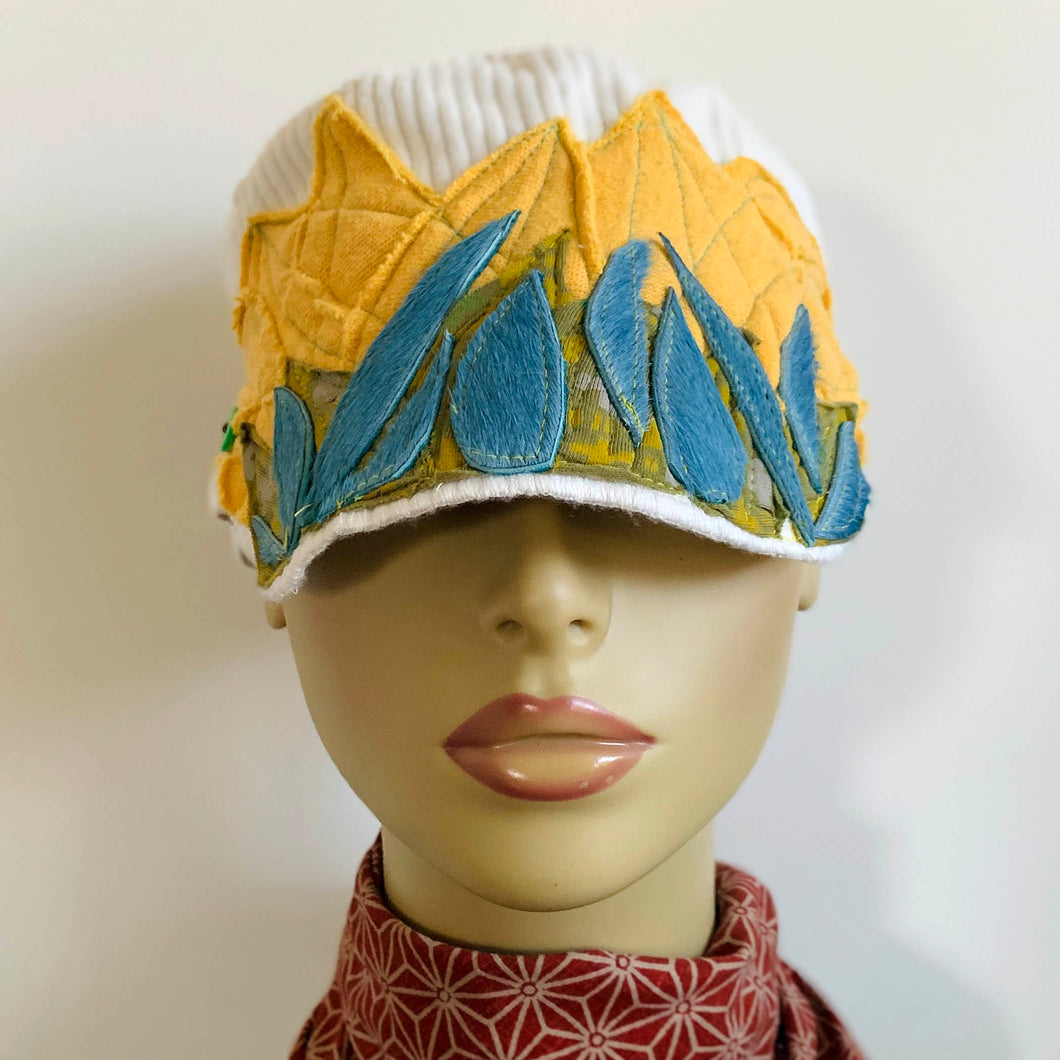 One of a kind design elements and embellishments upcycled from salvaged remnant fabric scraps, and hand sewn in Santa Cruz, CA. 100% cotton cap, handmade in Bali.   Yellow, blue and green elements  White ribbed cap One-of-a-kind Festive fire vibes Button and faux fur embellishments US size 7 5/8